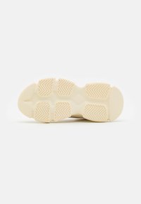 Semelle de sneaker beige clair avec une surface texturée, présentant un motif en chevrons répétitif et des bords arrondis pour une meilleure traction.