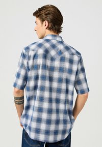 Sininen ja valkoinen lyhythihainen ruudullinen paita, jossa on nappikaulus ja teksturoitu kangas, jossa on hienovarainen ruutukuosi.