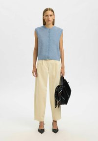 Šviesiai mėlynas be rankovių mezginys su mygtukų uždarymu, derinamas su šviesiai kreminėmis aukšto juosmens kelnių. Juoda rankinė su raštuota šaliku ir juodais aukštakulniais.