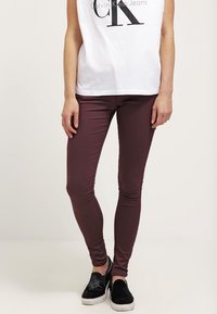 Jeans ajustados burdeos hechos de tela elástica, con un diseño entallado y combinados con zapatos negros tipo mocasín.