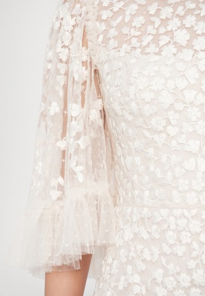 Detail čipkovaných šiat s vyšívanými kvetinovými vzormi, priesvitnými tylovými nafúknutými rukávmi a nariaseným lemom v jemných béžových tónoch.