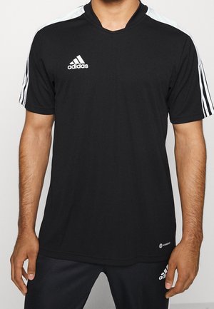 Mężczyzna w czarnej koszulce sportowej Adidas z białymi paskami na ramionach i rękawach, w połączeniu z czarnymi spodniami Adidas.