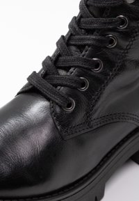 Černé kožené kotníkové boty s kulatou špičkou, texturovaným povrchem, kovovými očky a černými tkaničkami, s robustní podrážkou a bočním švem.
