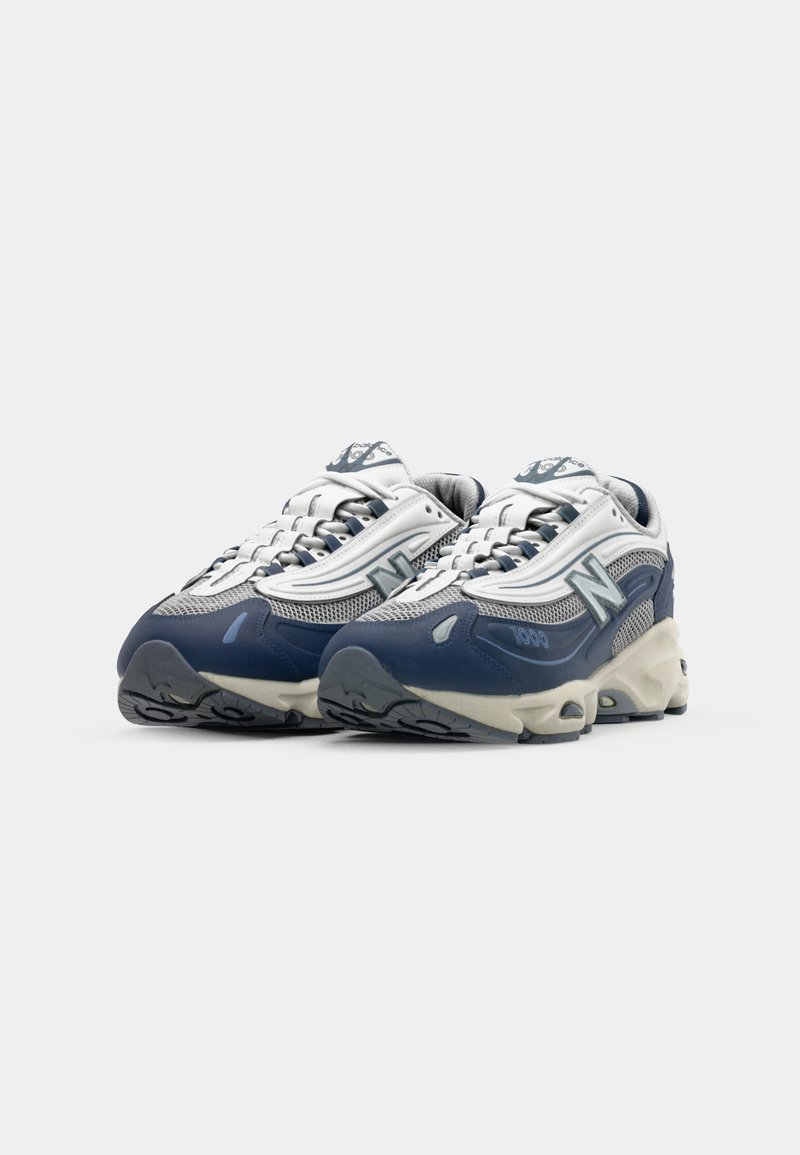 Zapatillas deportivas de color azul oscuro y gris con parte superior de malla y sintético, que destacan por una gruesa suela de color crema y acentos plateados en contraste.