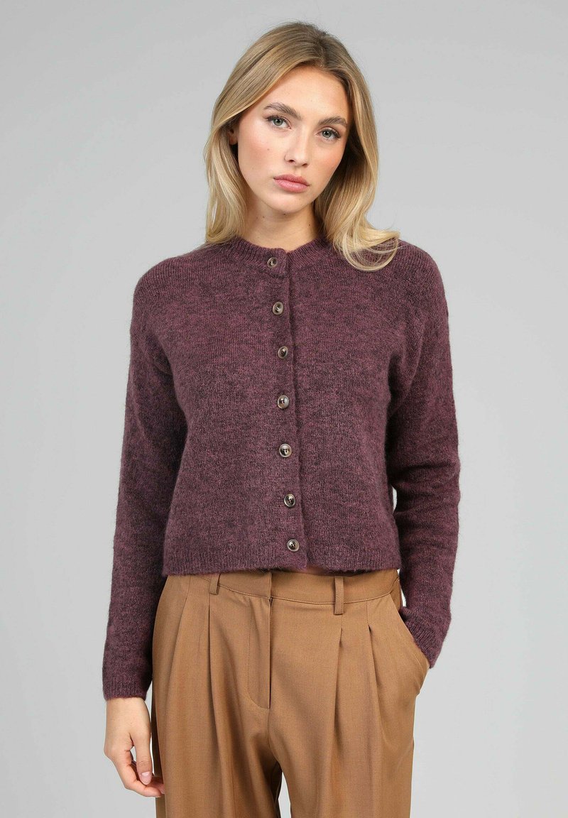 Cardigan en tricot bordeaux avec un col rond, sept boutons marron et des manches longues, associé à un pantalon beige plissé.
