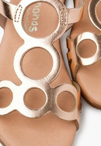 Metallisch goldene Sandalen mit runden Ausschnitten, mit einer glatten Oberfläche und einem braunen Fußbett. Leichtes Design, Gummisohle für besseren Halt.