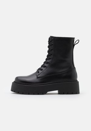 Schwarze Lederstiefeletten mit runder Zehenpartie, Schnürung vorne und einer dicken Gummisohle mit strukturiertem Profil. Mit Zugschlaufe an der Rückseite.