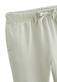 Pantalons rayés vert clair avec une taille élastique, un cordon de serrage ajustable et des poches latérales. Le tissu a une finition douce et texturée.