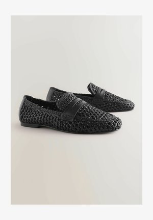 Sorte vævede loafers med tekstureret materiale, flad sål og et glat sort læderbånd over toppen.