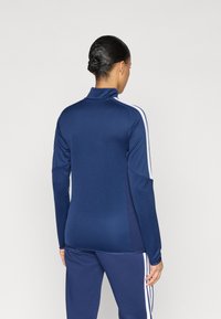 Ναυτικό μπλε αθλητικό μπουφάν με φερμουάρ, λευκές ρίγες στο πλάι, ελαστικό υλικό, ψηλό γιακά και εφαρμοστή γραμμή. Συνδυάζεται με παντελόνι στον ίδιο χρωματικό τόνο.