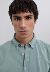 Lys grøn knap-opp skjorte med en blød tekstur, der har en spidse krave og et subtilt logo på brystet.