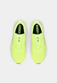 Ζευγάρι από νέον κίτρινα αθλητικά παπούτσια Hoka με λευκές σόλες και μαύρα πάτοι, σε θέαση από πάνω πάνω σε λευκό φόντο.