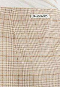 Tessuto a quadri beige con check marroni chiari e scuri. Presenta un'etichetta con "PATRIZIA PEPE". Superficie testurizzata, design sartoriale.