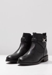 Black leather ankle boots with a smooth texture, featuring an ankle strap and silver hardware accents. Low block heel, rounded toe design.