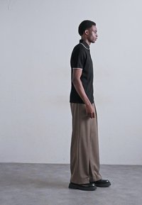 Cămașă polo neagră cu margine albă la guler, asortată cu pantaloni bej lejeri și pantofi cu platformă negri. Textură de bumbac netedă și croială confortabilă.
