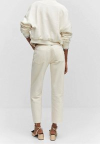 Pantaloni di cotone color crema con gamba dritta, tasche posteriori e orlo sfilacciato. Indossati con una felpa bianca a trama e sandali con tacco a blocco.