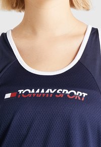 Canotta atletica blu navy con rifiniture bianche e tessuto in rete traspirante. Logo "TOMMY SPORT" in rosso e bianco sul petto.