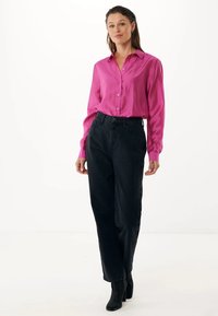 Camisa de botones fucsia de manga larga, combinada con pantalones negros de cintura alta con botones laterales y botas de tobillo negras con textura.