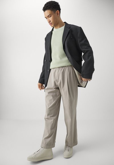 Svart blazer, lys grønn ribbestrikket genser, beige folderbukser og hvite sneakers. Glatte teksturer med en skreddersydd passform og minimalistisk design.