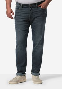 Vaqueros de mezclilla oscura de corte recto, con un diseño clásico de cinco bolsillos y un ligero efecto de desgaste. Combinados con zapatillas de color claro.