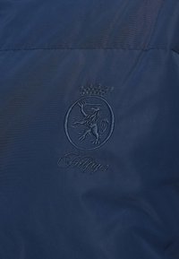 Mornarskoplavi materijal s glatkom teksturom, s izvezenim kružnim logotipom lava i natpisom "Hilfiger" ispod.