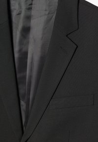 Schwarze Blazer aus einem glatten, strukturierten Stoff. Verfügt über einen geknöpften Reverskragen, eine einzelne Brusttasche und minimalistische Nähdetails.