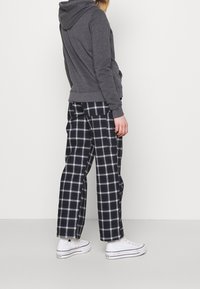 Grå huvtröja med avslappnad passform, kombinerad med svart-vita rutiga vida byxor och vita sneakers.