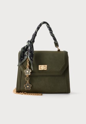 Olivgrüne Handtasche mit goldenem Verschluss, floraler Anhänger, schwarz gemusterter Schal am Griff gebunden und goldfarbener Kettenriemen auf weißem Hintergrund.