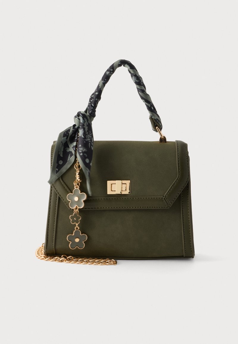 Sac à main vert olive avec fermoir doré, breloque florale, foulard noir à motif noué à la poignée et bandoulière chaîne dorée sur fond blanc.