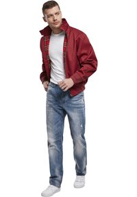 Veste bomber rouge avec doublure à carreaux, t-shirt blanc, jeans distressed bleu clair et baskets blanches, présentant un look décontracté en superposition.