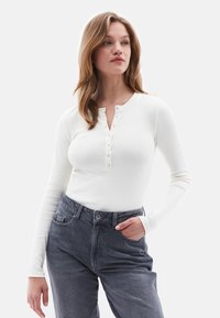 Witte longsleeve top met een geribbeld textuur, voorzien van een henley-nek, drukknoopjes, gecombineerd met donkergrijze high-waisted jeans.