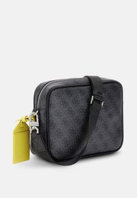 Borsa a tracolla sintetica nera con motivo, chiusura a zip, tracolla regolabile e un tag giallo accattivante attaccato. Texture liscia, forma rettangolare.