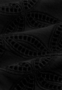 Črn material z zapletenim izvezenim cvetličnim vzorcem in izrezi, ki prikazuje teksturo in dimenzionalno šivanje.