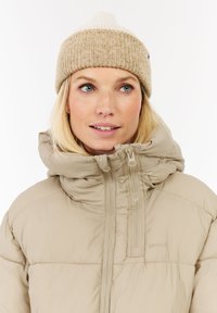 Beige donsjacket met hoge kraag en dubbele rits. Zachte, gladde textuur. Lichtbruine gebreide muts met een ribbelpatroon en platte bovenkant.