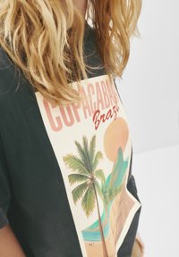 Temnozelena bombažna majica z retro grafiko Copacabane v Braziliji, ki prikazuje palme, sončni zahod in obalno pokrajino v mehkih barvah.