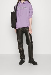 Osoba w lawendowej bluzie Bench, czarnych spodni faux skórzanych, czarnych loafersach i niosąca dużą czarną torbę na ramieniu.