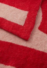 Coperta in lana rossa e beige con una trama morbida, caratterizzata da audaci forme geometriche e un design di bordo a contrasto.