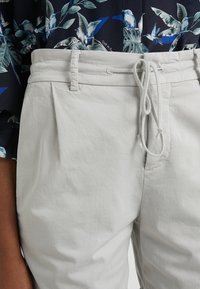 Ljust grå byxor med en avslappnad passform, med dragsko i midjan, veck fram och en mjuk bomullstextur.