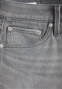 Grå denimjeans med en texturerad yta, försedda med silverfärgad hårdvara och en liten framficka. Sömmar är synliga längs kanterna.