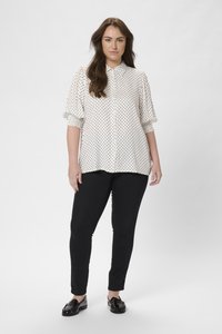 Chemise blanche à boutons avec des pois noirs, dotée de manches bouffantes. Associée à un pantalon slim noir et des mocassins noirs brillants.