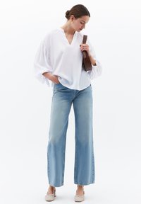 Blusa bianca, dalla vestibilità ampia, con scollatura a V e maniche arricciate abbinata a jeans a gamba larga di colore azzurro chiaro e scarpe slip-on beige.