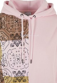 Hettegenser med en rosa ensfarget overdel og en brun, gul og hvit mønstret underdel med utsøkte design. Snorer og metallagn inkludert.