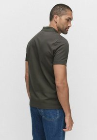 Olivgrön pikétröja med korta ärmar, tillverkad av ett slätt tyg. Kombinerad med blå jeans, vilket ger en enkel och avslappnad stil.