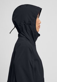 Zwarte capuchonjack met een gladde, matte afwerking. Heeft een strakke capuchon, gestroomlijnde silhouet en verborgen ritsdetails.