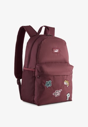 Bordowy plecak z tkaniny z zamykanymi na zamek komorami, przednia kieszeń z naszywkami oraz siatkowa kieszeń boczna na dodatkowe akcesoria.