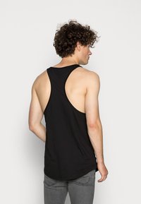 Svart bomullstopp med racerback-design, med avrundet hem og en glatt tekstur. Brukt sammen med grå jeans.