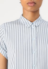 Camicia a righe blu chiaro con colletto, maniche corte e chiusura a bottoni con bottoni blu chiaro e sottili righe blu navy.