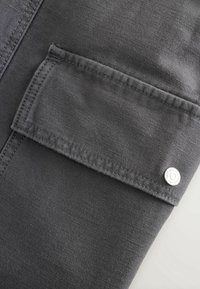 Gros plan d'une poche en tissu gris foncé avec rabat et bouton-pression en métal sur un vêtement.