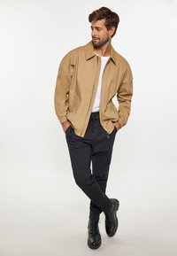 Hellbeige Bomberjacke mit einem Frontreißverschluss, kombiniert mit schwarzen Cargo-Hosen und schwarzen Schnürstiefeln. Glatte Textur und lässige Passform.