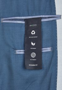 Blauter Stoff mit strukturiertem Muster und einem Etikett, das "H-ECO" anzeigt, mit Symbolen für recycelte Inhaltsstoffe, Nachhaltigkeit und Umweltfreundlichkeit.